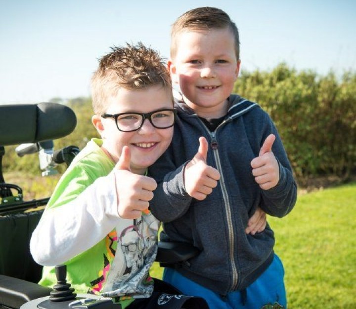 Two boys giving a thumbs up, one in a wheelchair