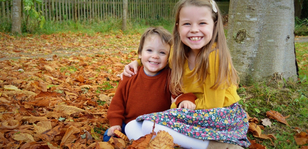 Girl and boy smiling sat in autumn leaves