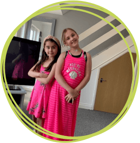 Two girls in pink dresses standing in their living room.