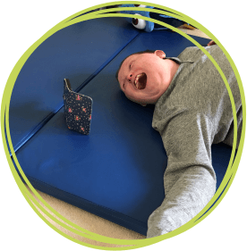 Boy laying on a rubber matt smiling watching a screen.