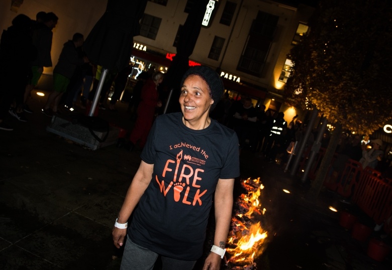Woman wearing black Firewalk t-shirt smiles as she finishes her walk along hot coals