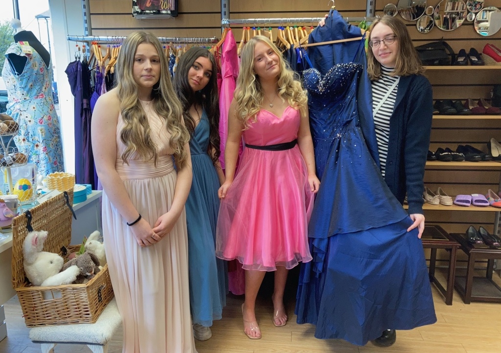 Honiton Community College students Ella-Mae Salter, Lian Galloen and Tia Rush try on some of the dresses with shop volunteer Emma Weir