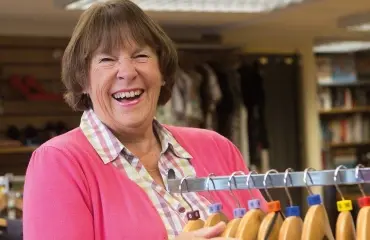 Smiling female volunteer in a shop next to a clothes rack CHSW Volunteer